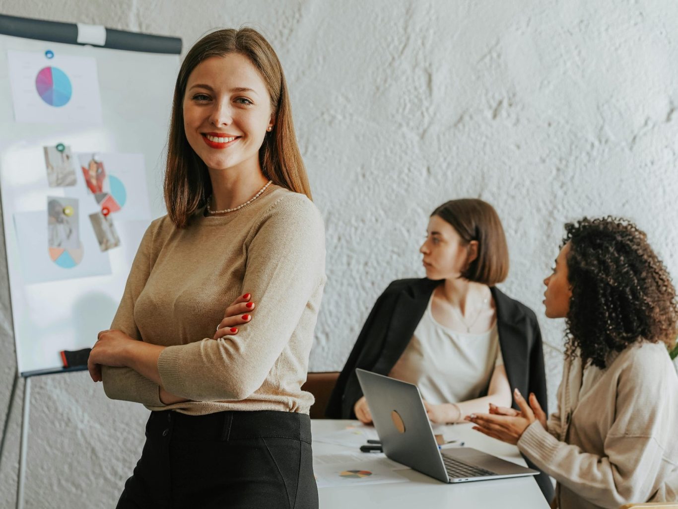 Marketing Frau in einem Meeting mit zwei Kolleginnen im Hintergrund, die diskutieren.